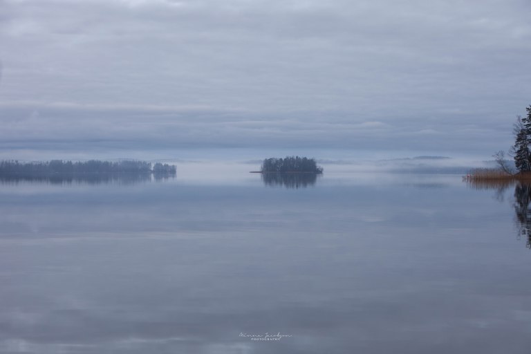 Lake in dense mist on Christmas Eve in Lohja, Finland, island appearing to float in soft diffused light.